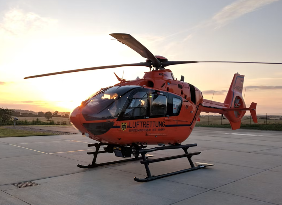 Oranje reddingshelikopter op een platform bij zonsondergang